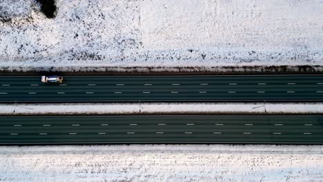 Winter-aerial-view-of-a-semi-truck-with-a-white-trailer-driving-on-a-snowy-highway,-with-multiple-cars-driving