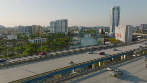 forwards fly above busy multilane highway in city. revealing luxury yacht passing on river and heading to lifted bridge. miami, usa