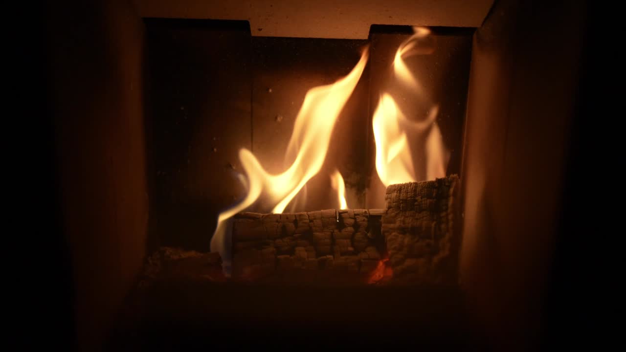 Closeup of firewood burning inside home fireplace with flickering flames in slow motion.