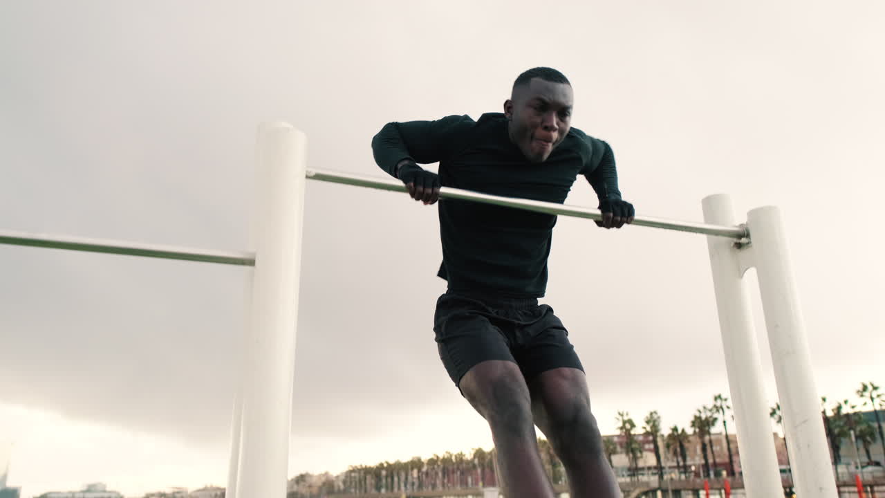 Uomo di colore determinato che esegue un muscle up su una sbarra sulla spiaggia.