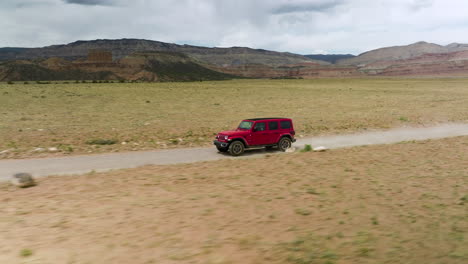 Jeep-Wrangler-Rojo-Conduciendo-Rápido-Por-Un-Camino-De-Tierra-A-Través-Del-Desierto-Semiárido-En-Utah,-Estados-Unidos