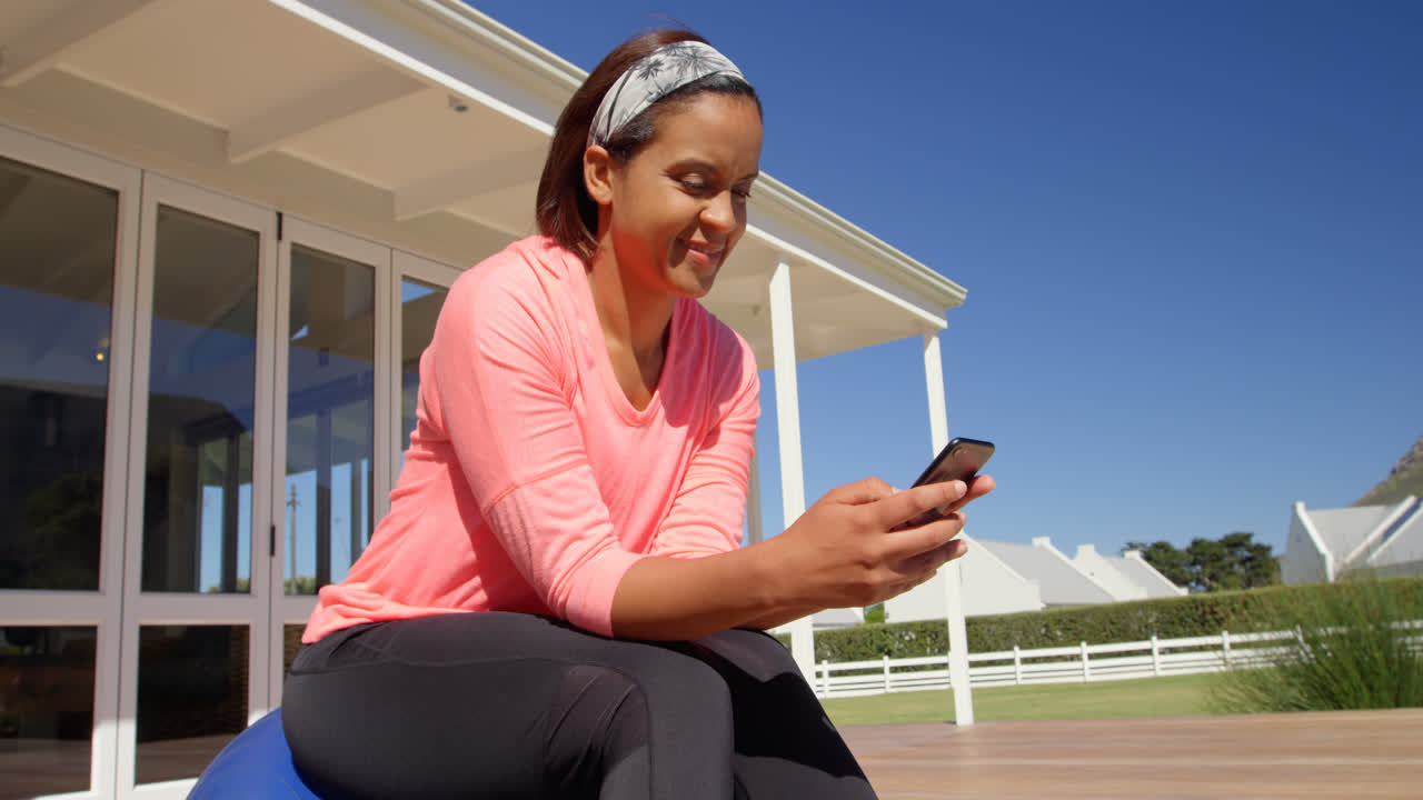 vista de bajo ángulo de una mujer madura de raza mixta usando un teléfono inteligente en el patio trasero de su casa 4k