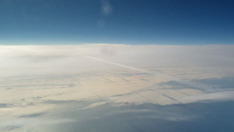 vista increíble desde la cabina de un avión que vuela alto por encima de las nubes dejando un largo rastro de aire de vapor de condensación blanco en el cielo azul
