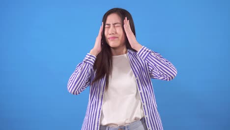 una hermosa joven asiática tiene dolor de cabeza sobre un fondo azul