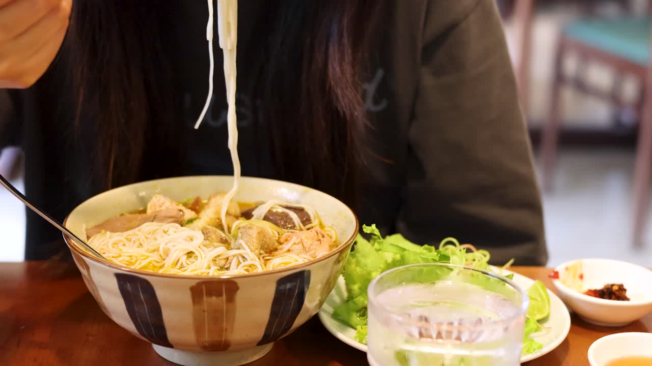 Một người phụ nữ dùng nĩa để gắp bún từ một bát bún đang bốc hơi