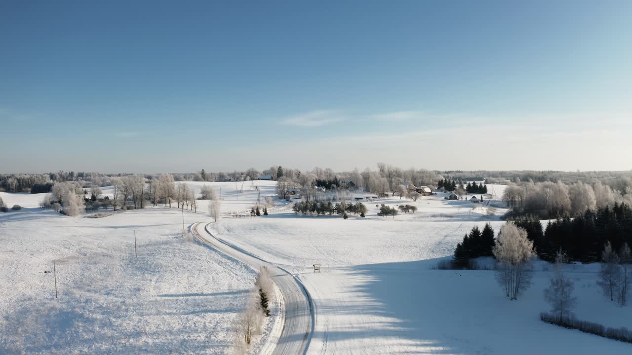 Rural area with family houses in winter season. Aerial view of winding snow road in countryside landscape. Early morning sunrise with hoar frost on the trees.