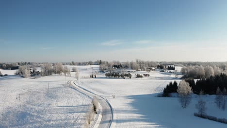 rural area with family houses in winter season. aerial view of winding snow road in countryside landscape. early morning sunrise with hoar frost on the trees.