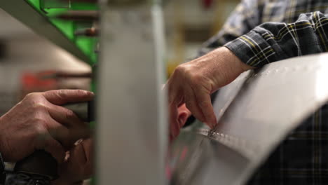 two workers assembling a large metal sheet, using specialized tools to secure the structure in place