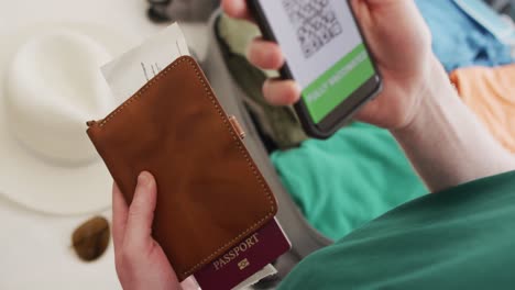 albino african american man holding smartphone with covid 19 vaccine passport