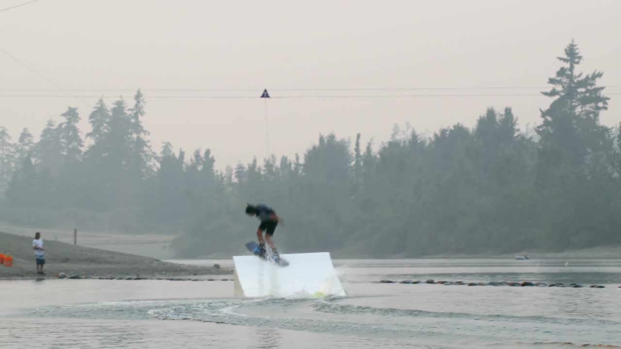joven caucásico haciendo trucos en wakeboard en el lago de la ciudad 4k