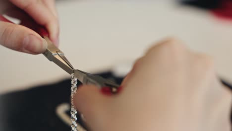 hands of person using tools to fix silver bracelet, close up view