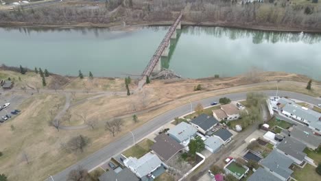 Luftaufnahme-Aus-Der-Vogelperspektive-über-Den-Verschmutzten-North-Saskatchewan-River-Im-Rundel-Park,-Vorbei-An-Einer-Leeren,-Ruhigen-Fußgängerbrücke-Bei-Parkhäusern-Während-Der-Covid-19-Beschränkung,-Wo-Soziale-Distanzierung-Praktiziert-Wird