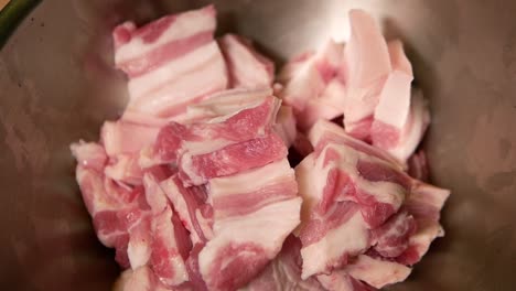 adding raw pork belly into metal mixing bowl, close up