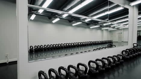empty gym with rows of kettlebells reflected in mirror
