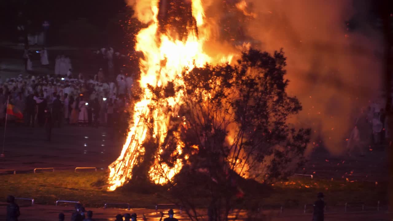 Close up shot for the tree burning and everyone is waiting for the cross to fall to know the direction