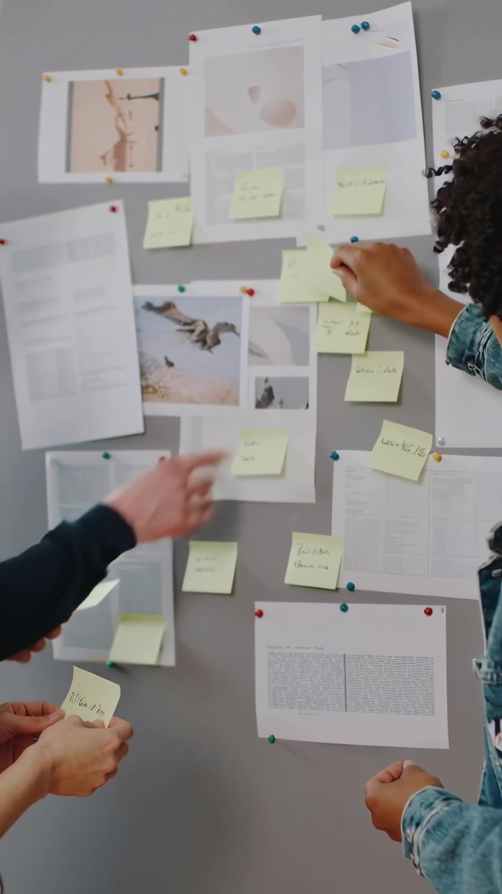 Vertical video: Peeling notes, team grouping clusters on pinboard with prints, denim, planning