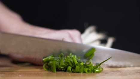 close up shot of lady cutting spring onions-scallions on cutting board with black background