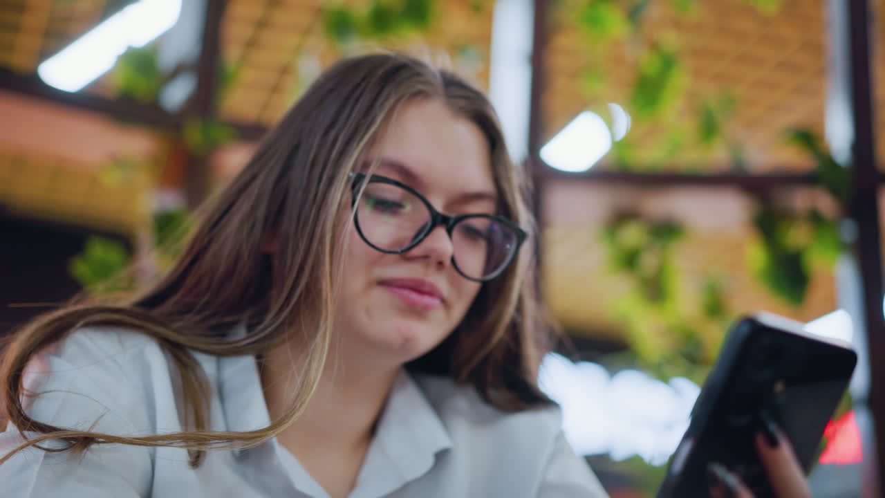 primer plano de una joven adulta sonriendo cálidamente mientras se ocupa de su teléfono, enmarcada por la vegetación borrosa en el fondo, añadiendo una atmósfera suave y tranquilizadora a su interacción