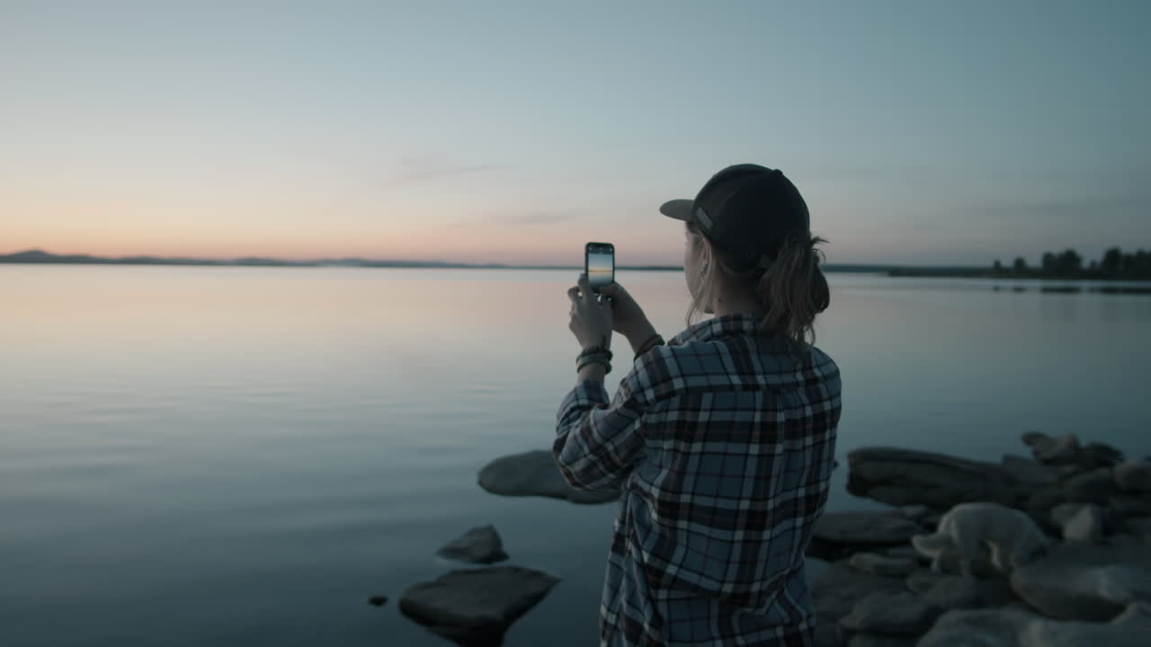 mujer tomando una foto del atardecer sobre el lago con un teléfono inteligente