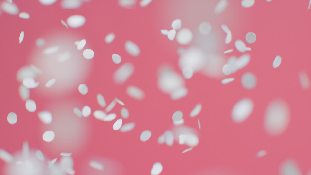 분홍색 배경에 떨어지는 흰색과 금색 색종이의 고정 샷