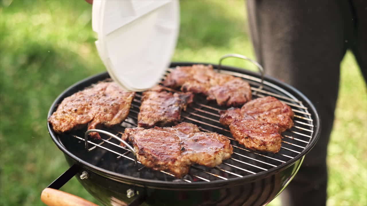 Young man frying meat on the grill. Greenery around. Glamping. Slow motion