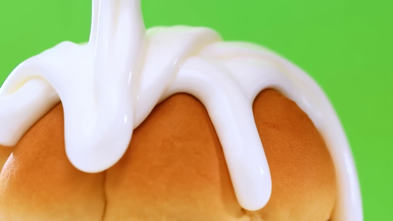 Primo piano di un panino morbido con glassa lucida che cola su un rotolo dorato caldo, contro uno sfondo verde vibrante, bianco denso.
