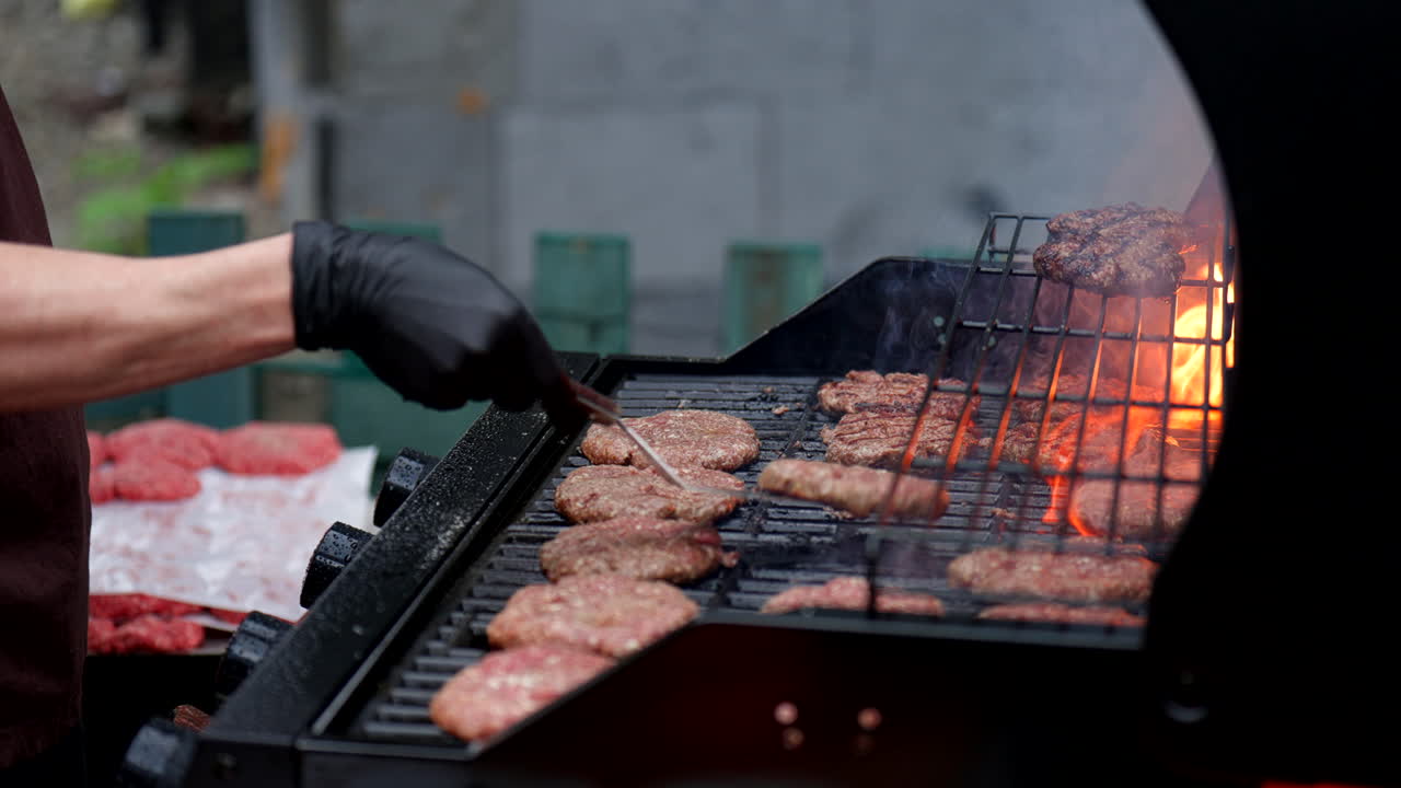 Juicy burgers cooking on an outdoor barbecue grill with open flames, smoke, and sizzle as a chef flips patties. Shot in 4K for commercial food and summer lifestyle use