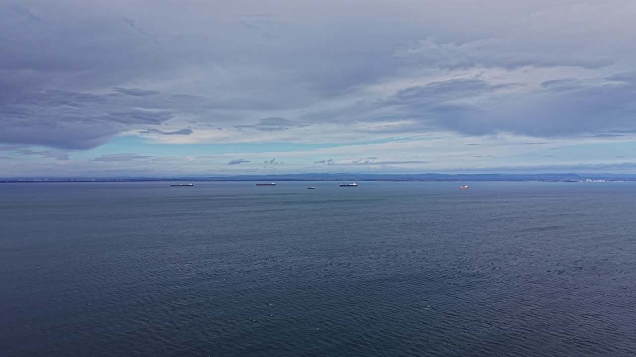 Skibe på vandet under en skyet himmel nær kystlinjen
