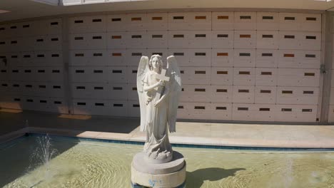 Close-up-panning-aerial-shot-of-the-statue-of-a-Catholic-angel-in-front-of-a-stone-mausoleum-at-a-mortuary-in-California