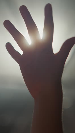 child hand silhouette at backlight. little kid bends fingers holding palm against glowing lamp in dark room. child plays with light beams closeup