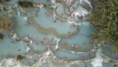 Drone-Descends-on-People-Relaxing-at-Cascate-del-Mulino,-Saturnia,-Tuscany,-Italy