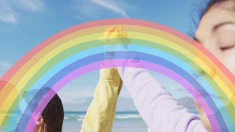 animation of rainbow over woman holding hands over beach