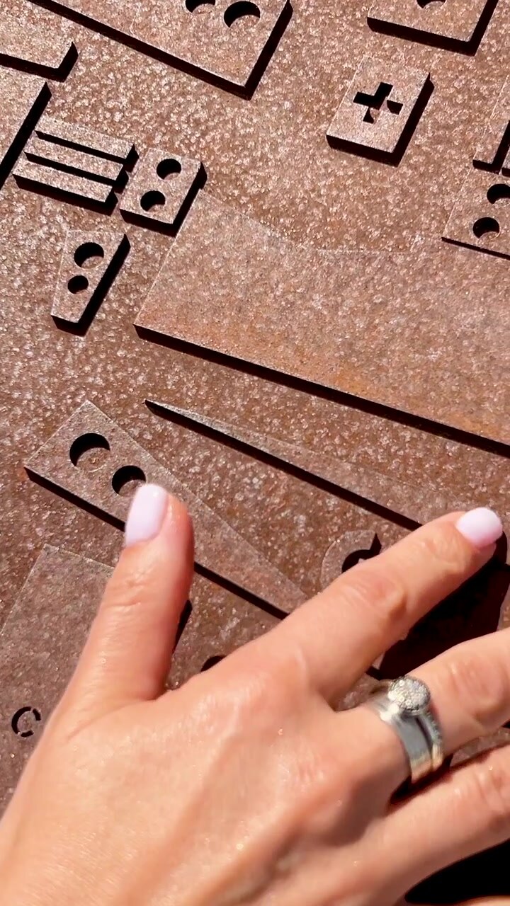 A womans hand with rings and pink manicure touches an industrial rusty metal surface with geometric cutouts and symbols. Cinematic vertical shot for mobile social media.