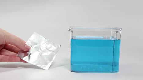 hands manipulate aluminum foil in water, demonstrating buoyancy principles with clear, bright lighting and a simple setup