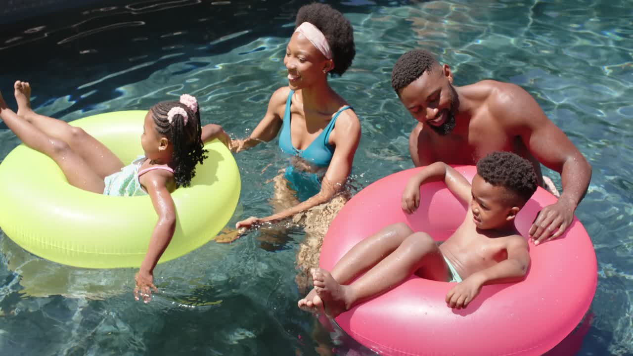 una feliz familia afroamericana con nadadores en la piscina, en cámara lenta.