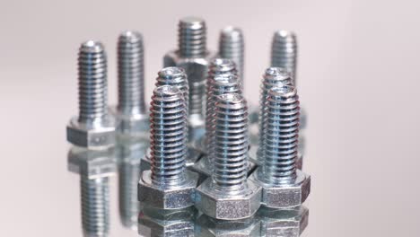 rotating group of galvanized metallic screws close-up. stainless steel bolts isolated on mirror reflective background.