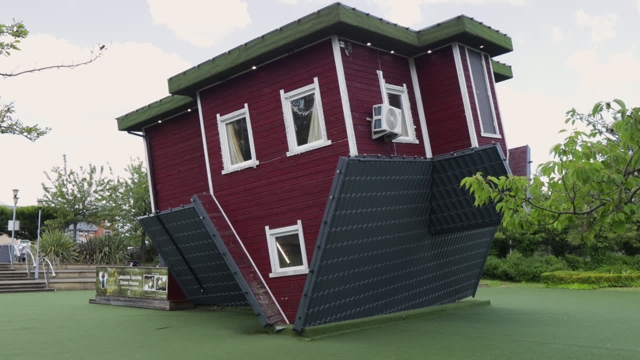 Upside-down red house with white trim and green roof in a park setting