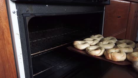 hands with oven mitts remove a tray of fresh baked bagels from home oven