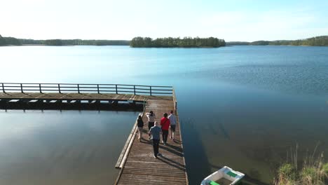 a family with a dog strolling on a pier with an island on the lake in the background