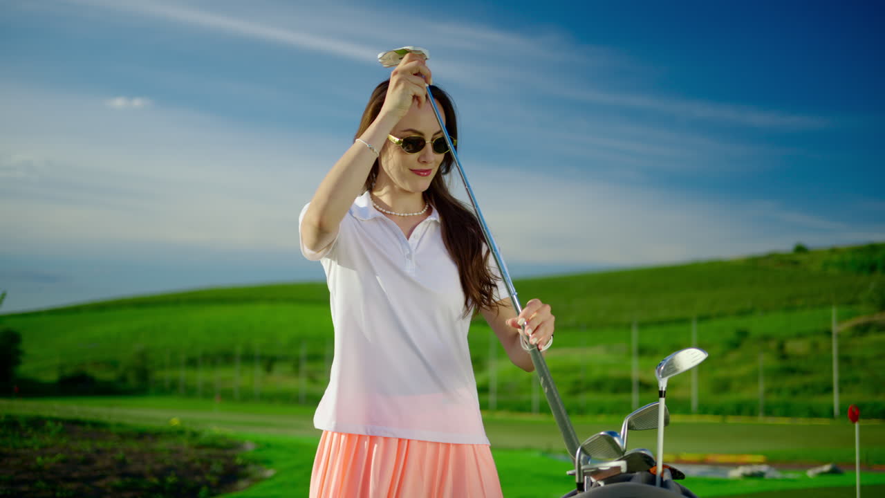 Woman dressed in white and pink putting a golf club in a cart bag on the course