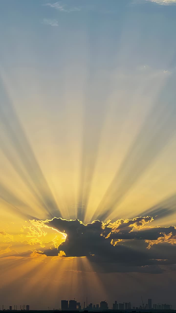 Vertical video: Sun descending behind central cumulus cloud casting widening rays over city skyline