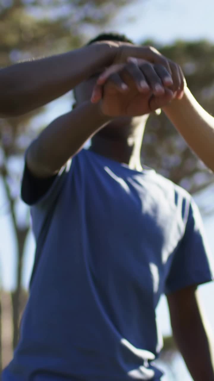 Vertical video: Stacking hands, lead boy calling team, raising arm at park for cheer in blue shirts