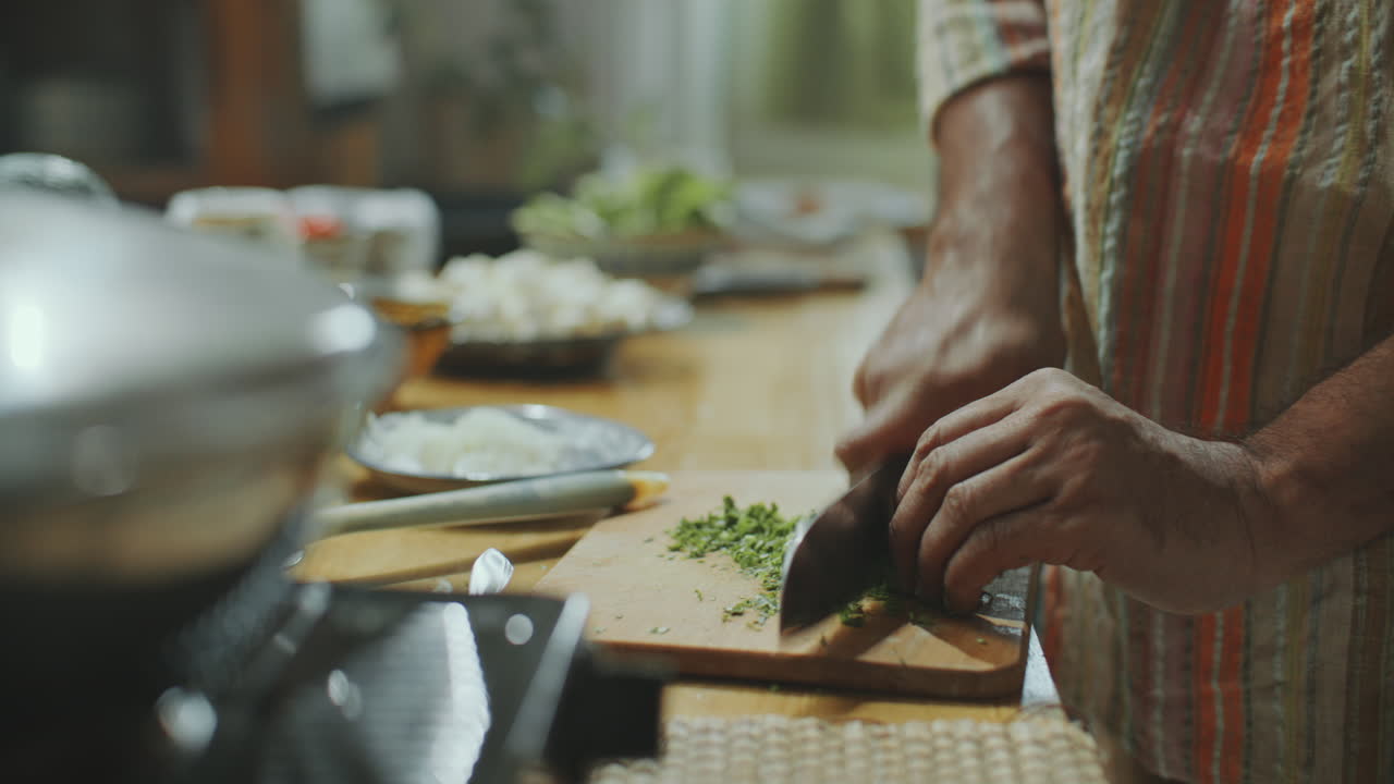 hombre indio mayor cortando hierbas frescas en una tabla de madera en la cocina