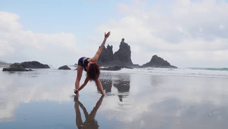 Engaging-in-slow-motion-stretching-and-yoga,-a-young-woman-stands-by-the-ocean's-edge,-gazing-into-the-distance-with-contemplation