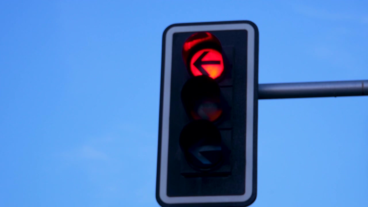 Un primer plano de un semáforo en rojo mostrando una flecha de giro a la izquierda contra un cielo crepuscular en España. Útil para temas de transporte urbano y seguridad vial