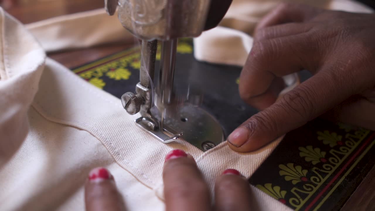 mujer india rural irreconocible cosiendo tela en una máquina de coser interior, primer plano, cámara lenta