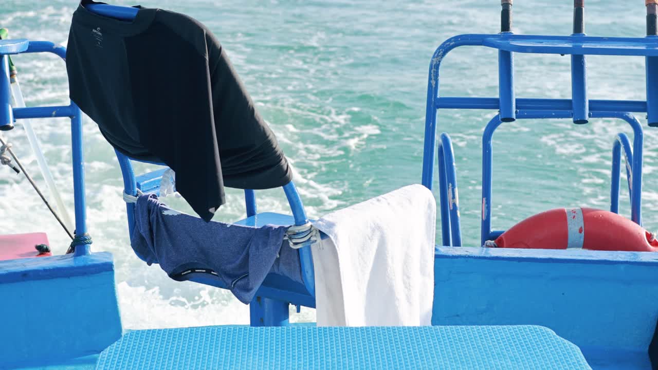 Clothes hang drying on a moving boat in Phuket, Thailand, with vibrant blue waters and bright daylight