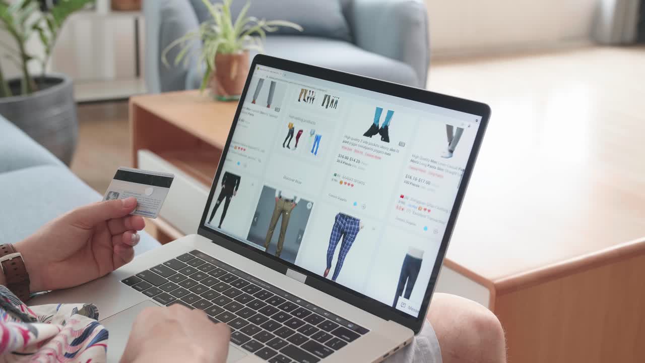 Close Up Of Hand Man Holding Credit Card And Looks At Goods In Online Store Clothing. Buy Fashion Clothes Directly On Laptop Computer