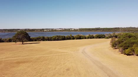 Large-blue-lake-in-background,-trees-and-ground-in-foreground,-Zoom-in