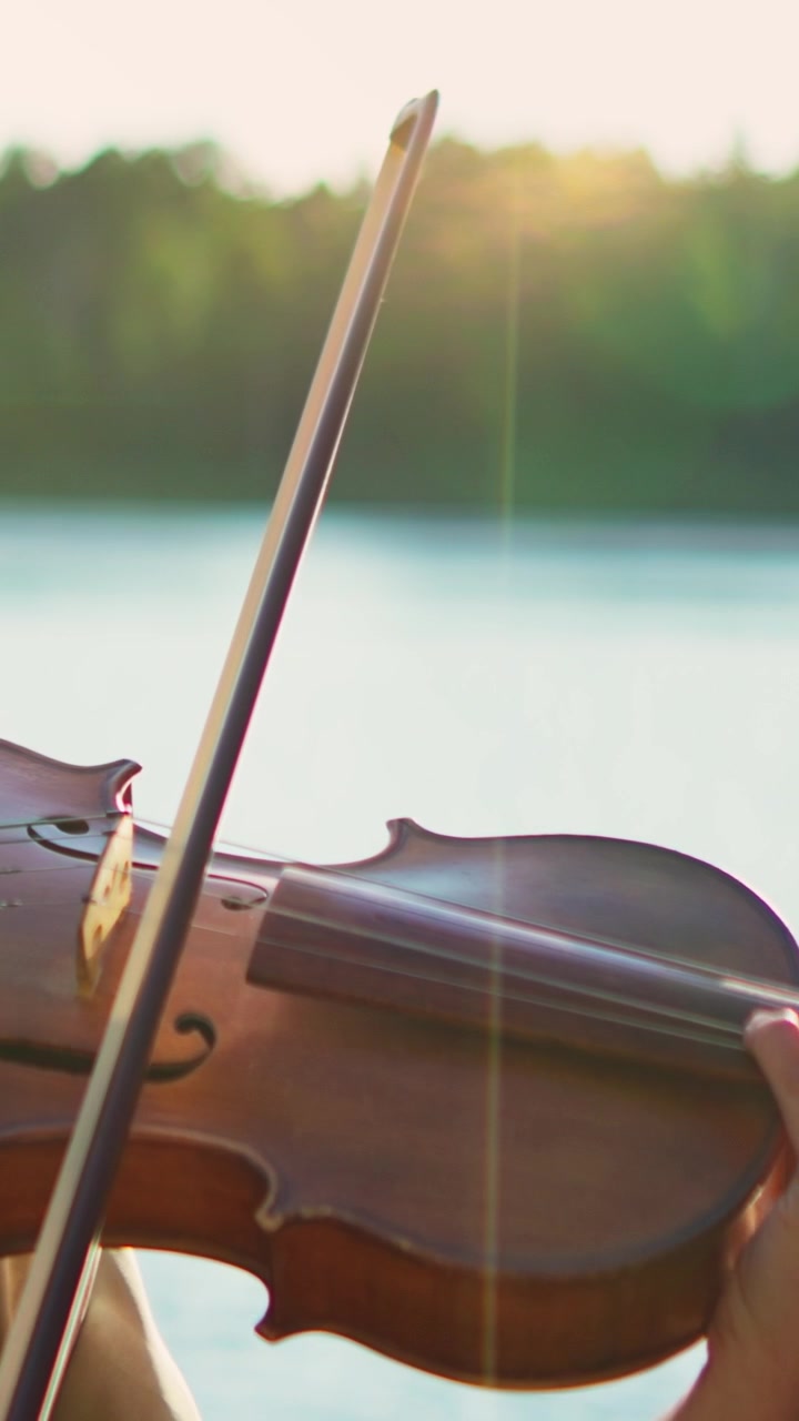 Woman Playing Violin Outdoors by a Lake at Sunset